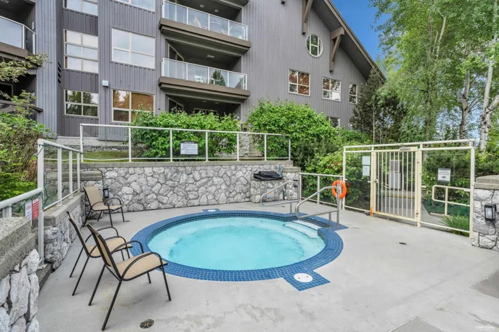 Outdoor hot tub with blue tile border, surrounded by a stone-clad retaining wall and glass panel railings