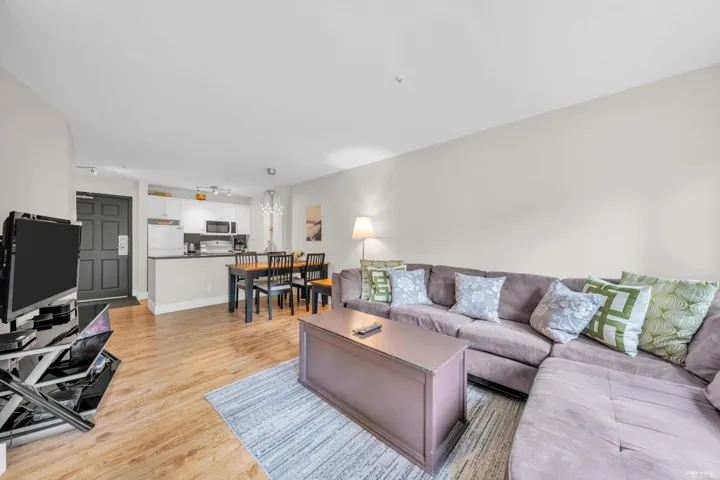 Open-concept living area featuring wood-finish flooring, a kitchen with white cabinetry and black appliances, and a dining area with a wood table