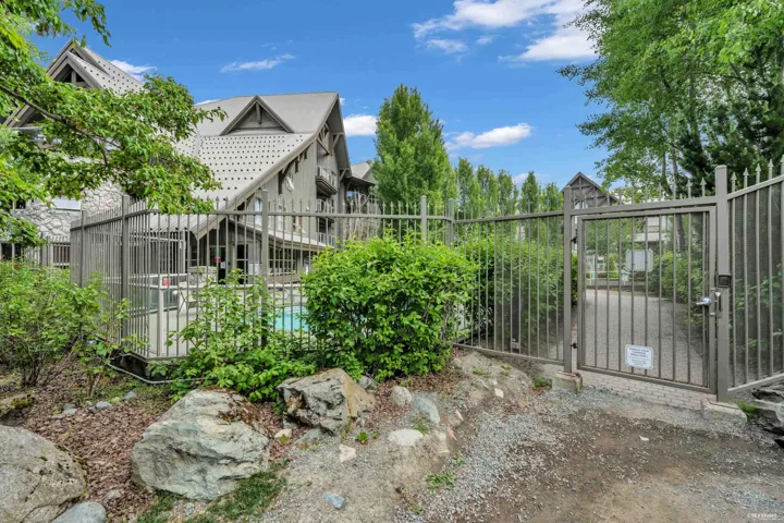 Gated entrance to a multi-story building featuring pitched roofs, stone accents, and a fenced pool area