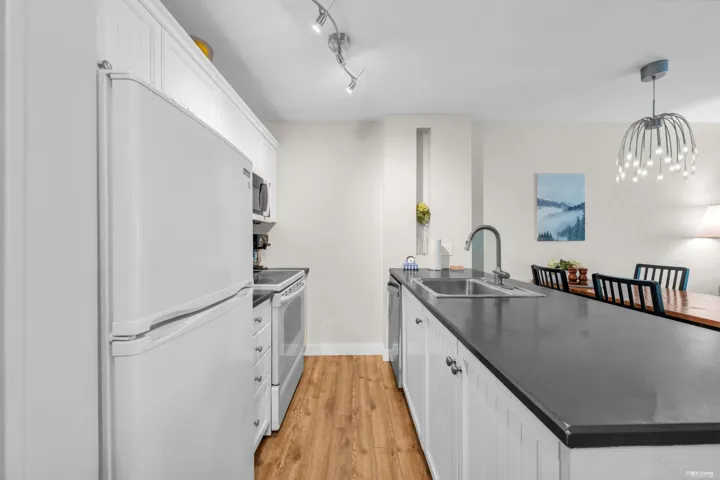 Kitchen featuring wood-finish flooring, white cabinetry with beadboard paneling, and a black countertop with an undermount double-basin sink