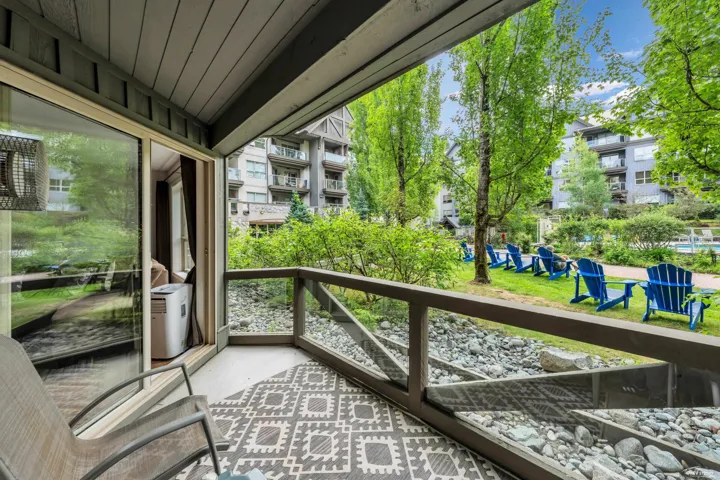 Private balcony featuring a geometric patterned outdoor rug, glass railing, and wood-finish ceiling