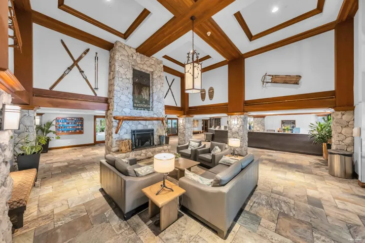Spacious common area featuring a stone-clad fireplace and pillars, wood-beamed ceilings, and natural stone flooring