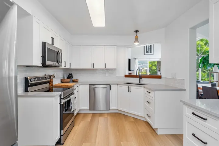 Kitchen featuring stainless steel appliances, backsplash, white cabinets, light wood-style floors, and pendant lighting