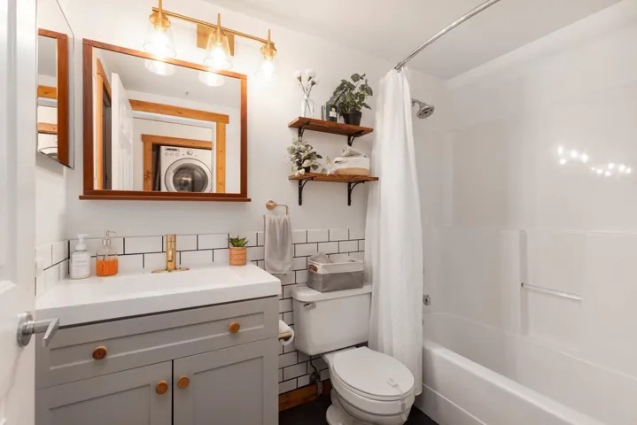 Bathroom with vanity, shower / bath combination with curtain, stacked washer / drying machine, tile walls, and toilet