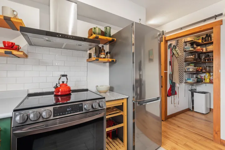 Kitchen with tasteful backsplash, light wood-style flooring, appliances with stainless steel finishes, island exhaust hood, and open shelves