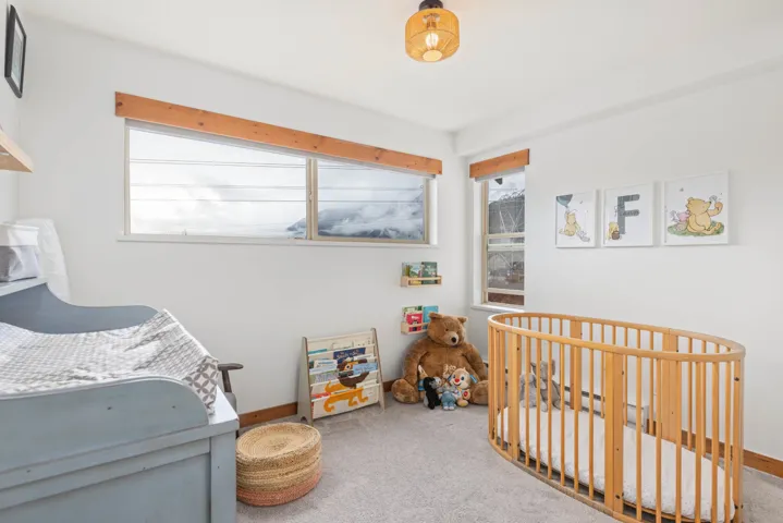 Carpeted bedroom with multiple windows, a crib, and baseboards