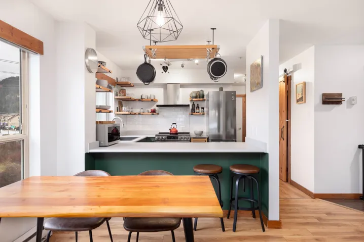 Kitchen with light wood-style flooring, appliances with stainless steel finishes, a barn door, wall chimney range hood, and tasteful backsplash