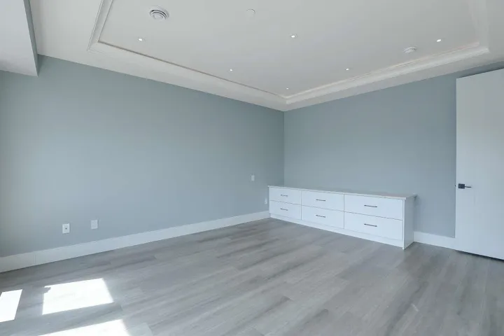 Empty room with light wood finished floors, a tray ceiling, and baseboards