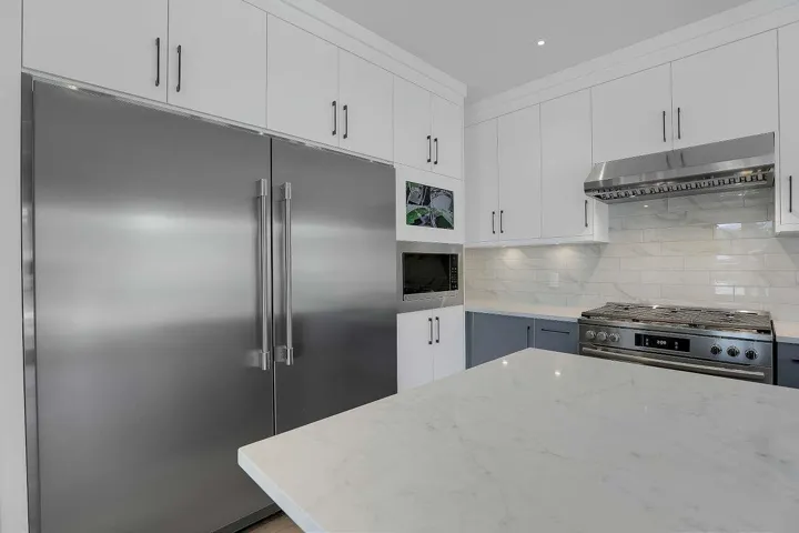 Kitchen featuring appliances with stainless steel finishes, ventilation hood, tasteful backsplash, light stone countertops, and white cabinets
