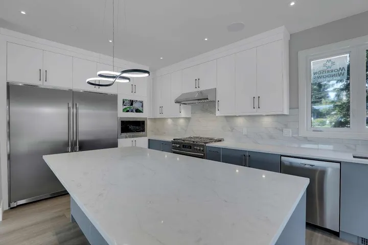 Kitchen with built in appliances, under cabinet range hood, decorative backsplash, light stone countertops, and light wood-style flooring