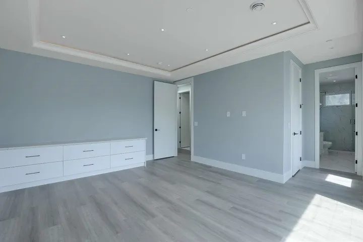 Unfurnished bedroom featuring a raised ceiling, light wood finished floors, connected bathroom, and recessed lighting