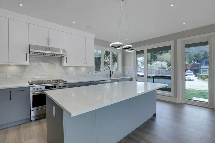 Kitchen with under cabinet range hood, stainless steel appliances, a center island, tasteful backsplash, and hanging light fixtures
