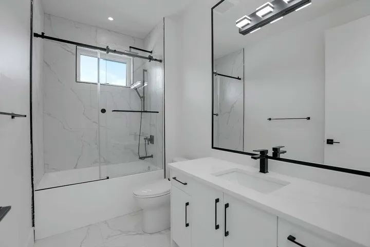 Bathroom featuring marble finish flooring, combined bath / shower with glass door, vanity, and toilet