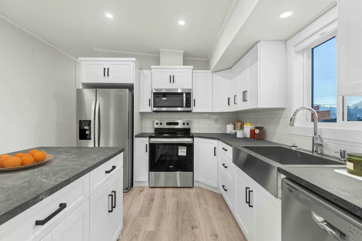 Kitchen with vaulted ceiling, stainless appliances, ample storage and work surface, white shaker style cabinets, and recessed lighting.  Photo has been virtually staged.