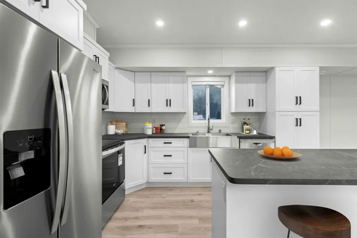 Kitchen with vaulted ceiling, stainless appliances, ample storage and work surface, white shaker style cabinets, and recessed lighting.  Photo has been virtually staged.