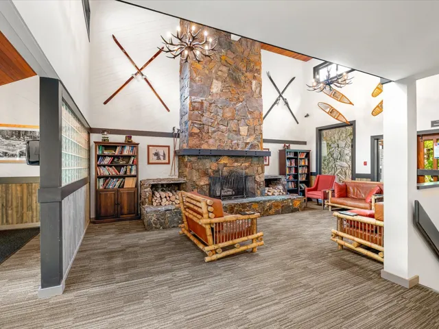 Carpeted living room featuring high vaulted ceiling, a stone fireplace, and a chandelier