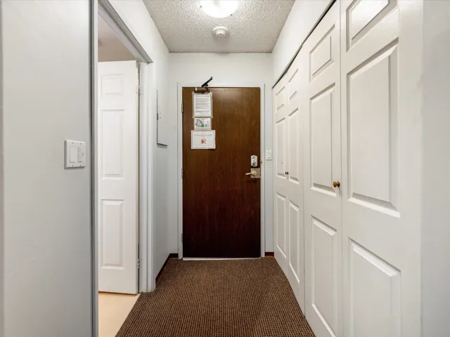 Hall with dark colored carpet and a textured ceiling