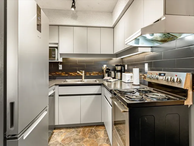 Kitchen with appliances with stainless steel finishes, under cabinet range hood, white cabinets, and stone finish floors