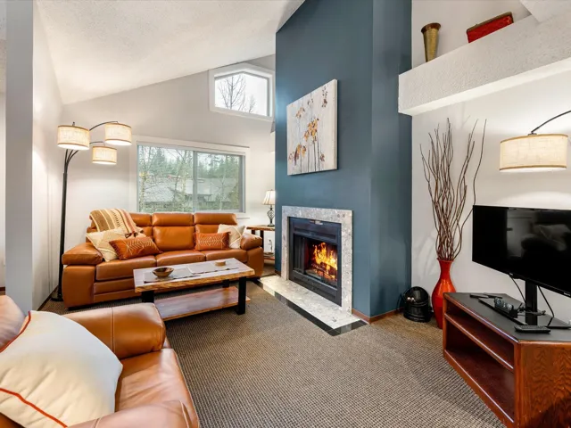 Carpeted living area featuring a fireplace with flush hearth and high vaulted ceiling