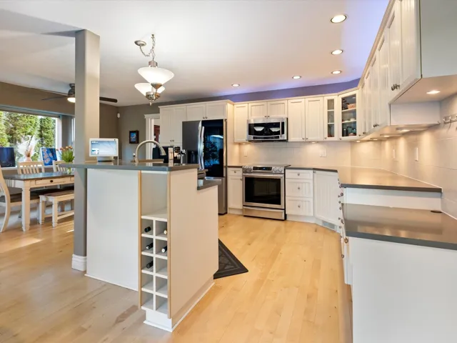 Kitchen featuring appliances with stainless steel finishes, dark countertops, light wood-style flooring, and tasteful backsplash