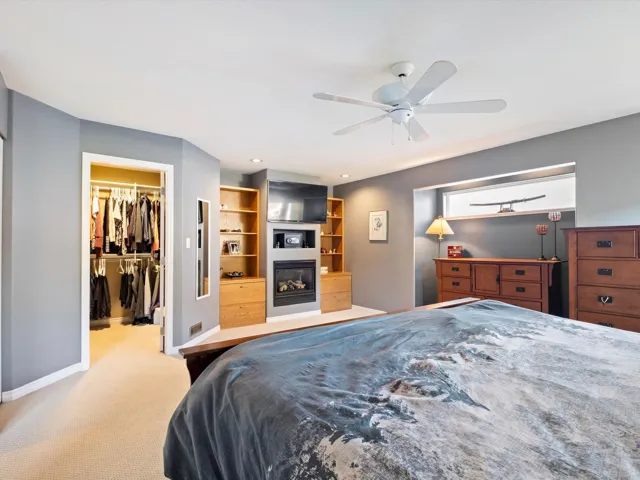 Bedroom featuring baseboards, a glass covered fireplace, ceiling fan, a spacious closet, and carpet floors