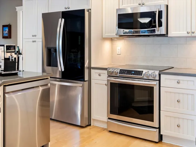 Kitchen featuring stainless steel appliances, dark countertops, backsplash, and light wood-style floors