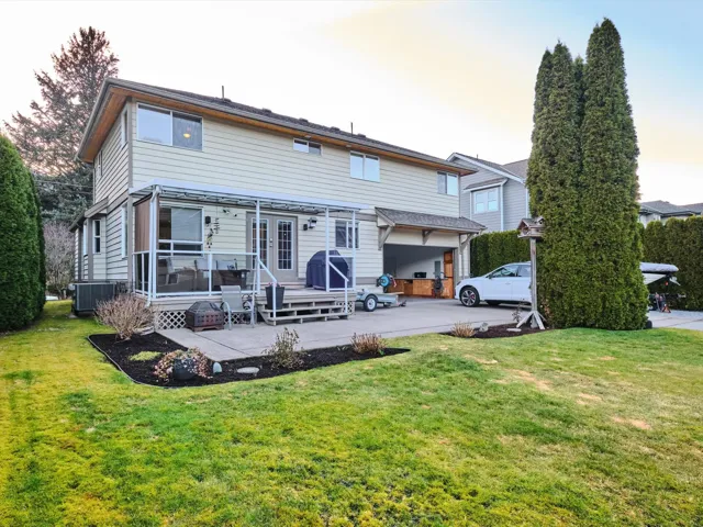 Back of property featuring concrete driveway, a patio area, a lawn, and central AC unit