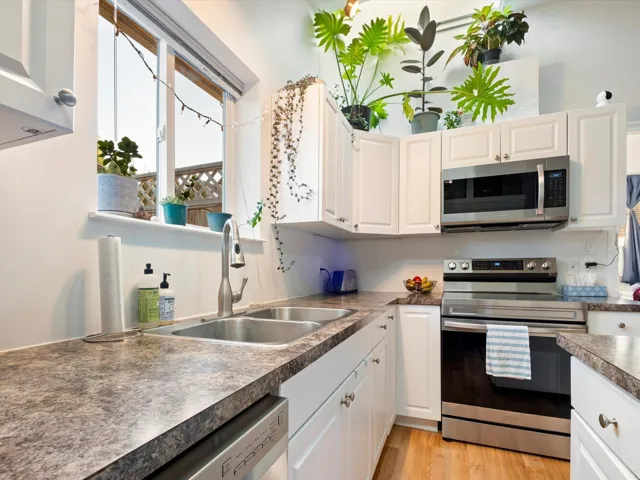 Kitchen with stainless steel appliances, dark countertops, light wood-style floors, white cabinets, and a sink