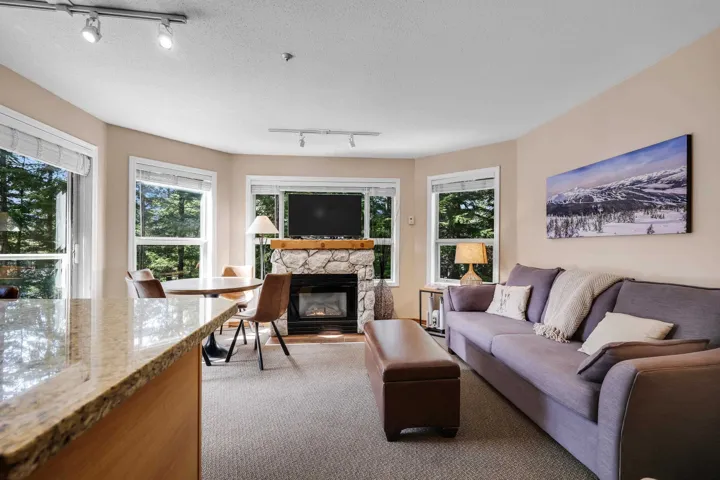 Living area with rail lighting, a stone fireplace, a textured ceiling, and light colored carpet