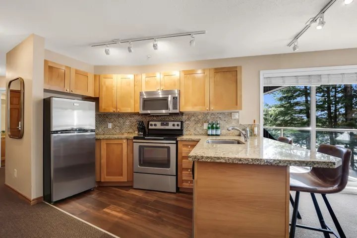 Kitchen with a peninsula, light stone countertops, stainless steel appliances, a breakfast bar area, and rail lighting