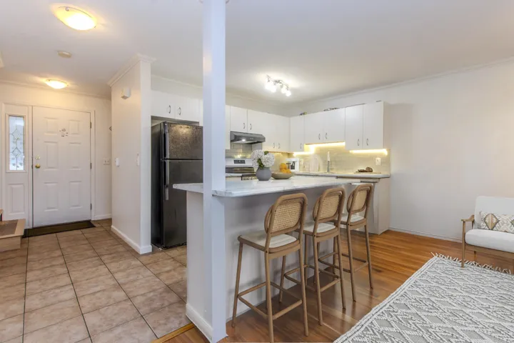 Kitchen featuring a kitchen breakfast bar, white cabinets, freestanding refrigerator, decorative backsplash, and crown molding