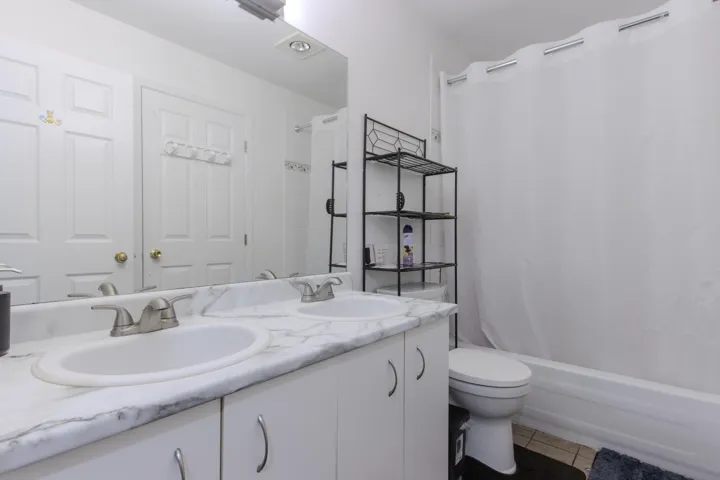 Full bath featuring double vanity, light tile patterned floors, and shower / tub combo with curtain