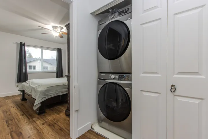 Washroom with dark wood-style floors, stacked washing machine and dryer, and a ceiling fan