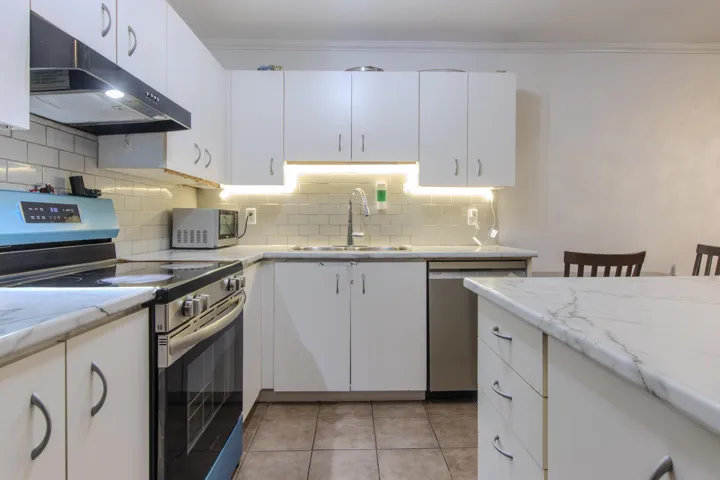 Kitchen with appliances with stainless steel finishes, under cabinet range hood, white cabinets, backsplash, and ornamental molding