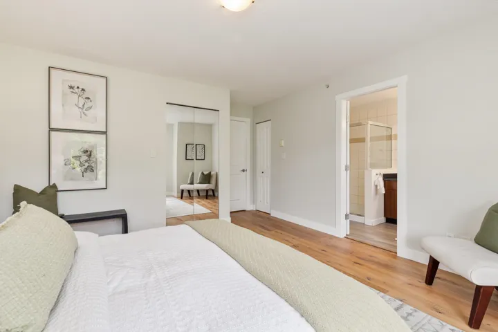 Bedroom with wood finished floors, baseboards, ensuite bath, and two closets