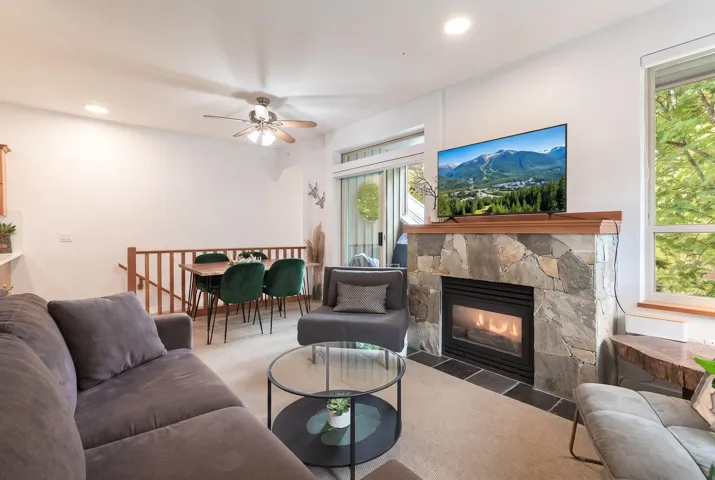 Living area featuring a stone-clad fireplace with a wood mantel, a large window, a ceiling fan, recessed lighting, and a dining area with wood railing