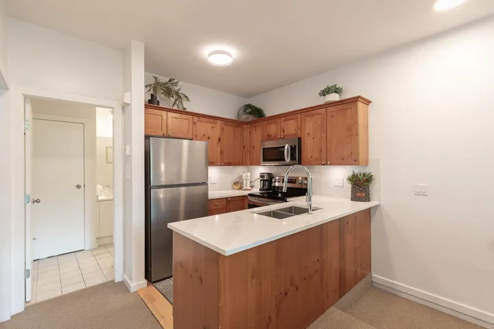 Kitchen featuring wood cabinetry, stainless steel appliances, white countertop, and a double basin sink with a high-arc faucet