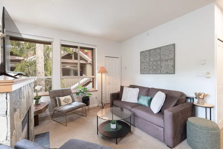Living area featuring an integrated stone fireplace with a natural wood mantel, large windows with natural wood trim, plush carpet flooring, and white walls