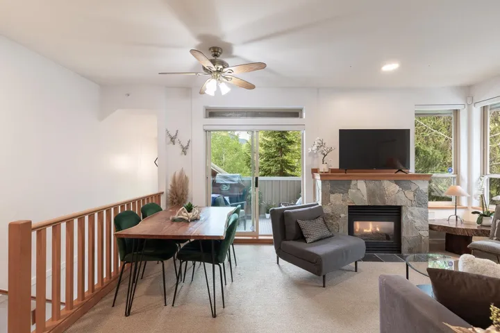 Open-concept living area featuring a stone fireplace with a wood mantle, a balcony with a glass sliding door, and multiple windows