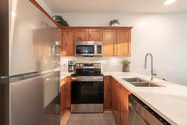 Kitchen featuring wood cabinetry, white countertops, a double basin stainless steel sink, and stainless steel appliances including a refrigerator, range, microwave, and dishwasher