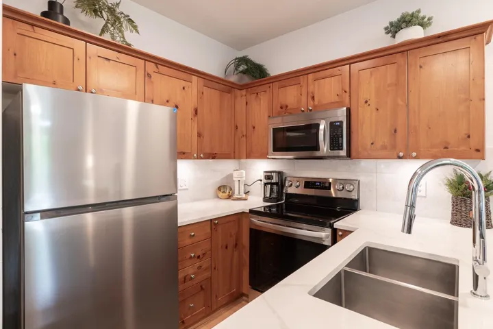 Kitchen featuring wood cabinetry, white countertops, stainless steel appliances, and a double basin sink with a chrome faucet