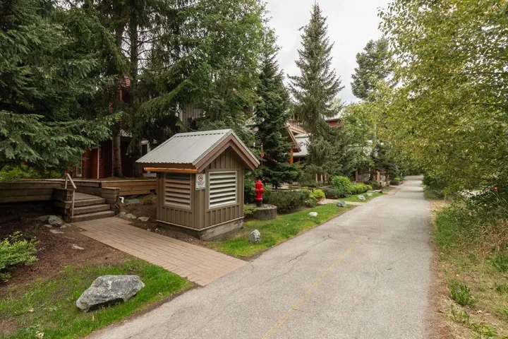 Paved pathway providing access to residences with wood siding, surrounded by mature trees and landscaping