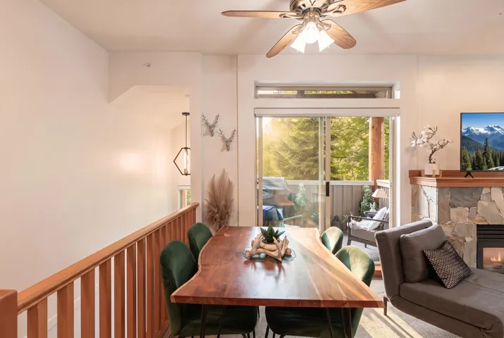 Living area featuring a natural wood-finish railing, a ceiling fan with integrated lighting, and a stone-clad fireplace with a natural wood mantel