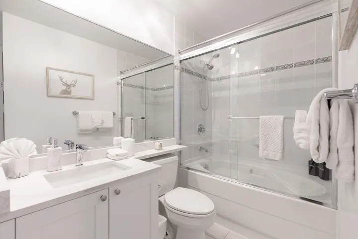 Bathroom featuring a white vanity with an integrated sink, polished chrome faucet, a large mirror, a toilet, and a combined bathtub and shower with glass sliding doors