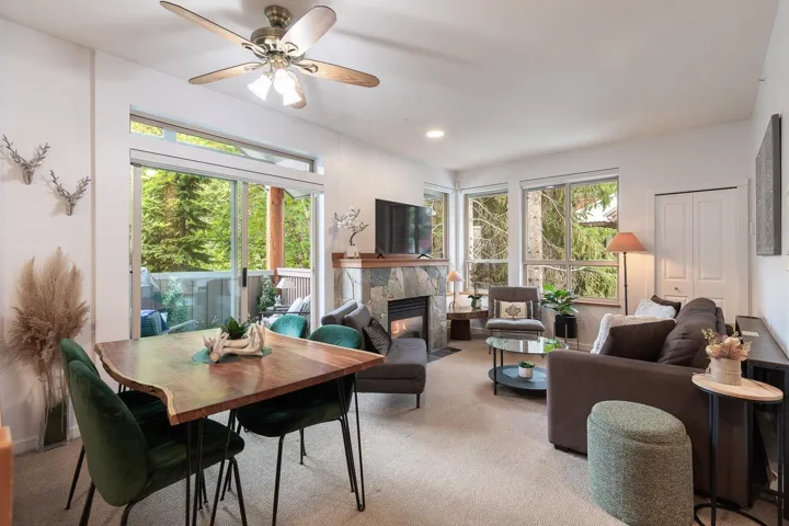 Living area featuring a stone fireplace, large windows, ceiling fan, and sliding glass door leading to a balcony