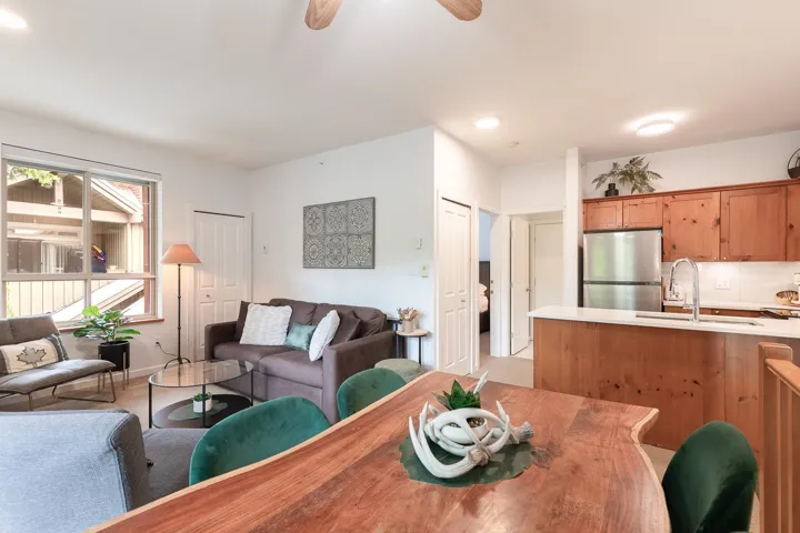 Open-concept living area featuring a kitchen with wood cabinetry and stainless steel appliances, a dining area with a natural wood-finish table, and a living room with wood-finish flooring
