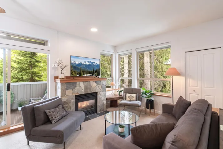 Living area featuring a stone-clad fireplace with a wood mantel, sliding glass door access to a balcony, multiple windows, and carpeted flooring