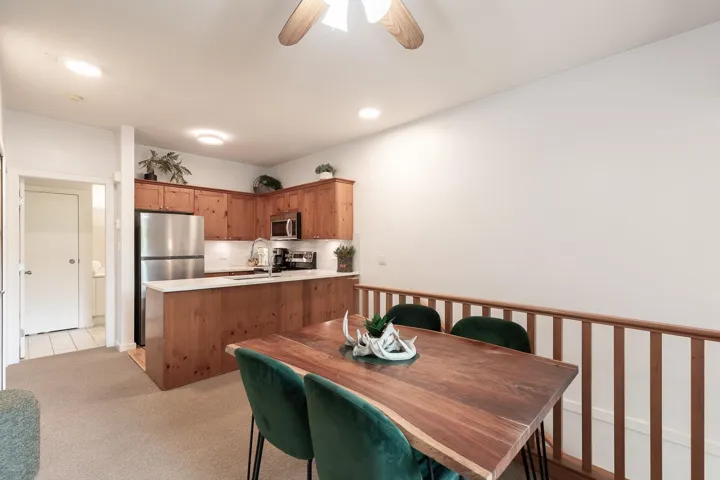 Open-concept dining and kitchen area featuring wood cabinetry, stainless steel appliances, white countertops, and a wood-finish dining table