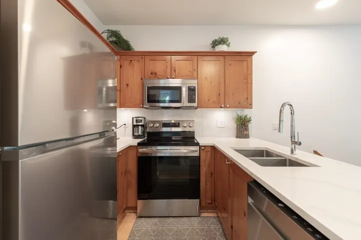 Kitchen featuring wood cabinetry, light-toned countertops, a stainless steel refrigerator, stainless steel range with overhead microwave, and a double basin sink with a high-arch faucet