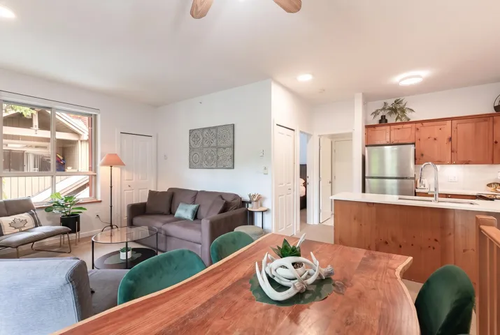 Open-concept living area with a natural wood dining table, stainless steel appliances, wood-finish cabinetry, a breakfast bar with solid surface countertop, and large windows